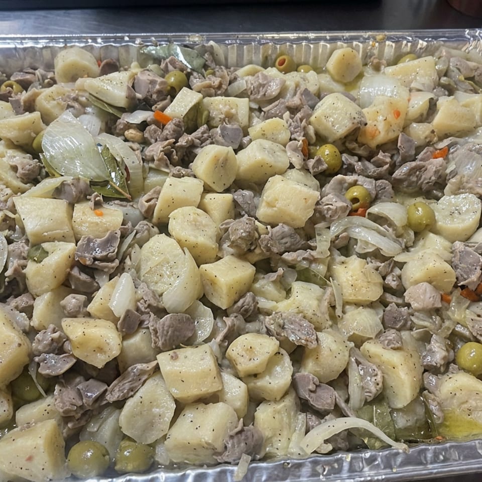 Aluminum catering tray filled with creamy potato chunks, sliced onions, green olives, mushrooms, and seasoned meat.