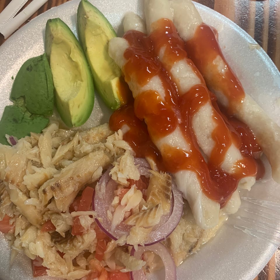 Plate of shredded chicken salad with tomatoes, red onions, avocado, and white tortillas drizzled with red sauce.