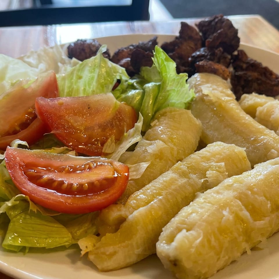 Plate of crispy fried rolls, dark grilled meat, and lettuce-tomato salad on a wooden restaurant table.