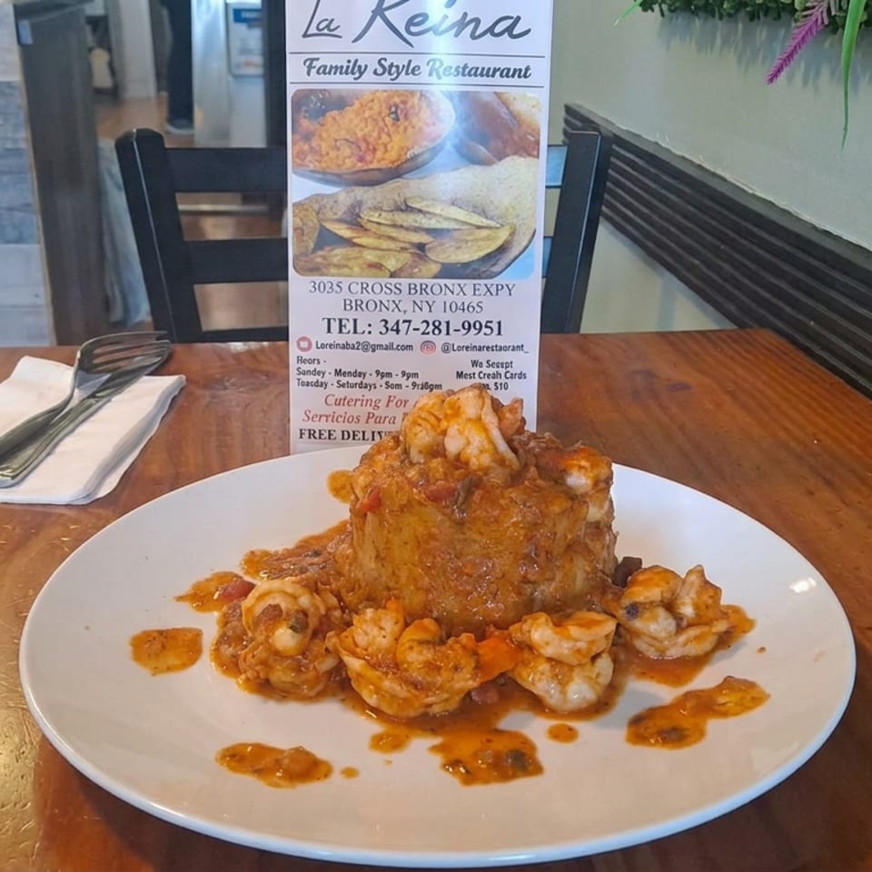 Mofongo topped with sauced shrimp and surrounded by additional shrimp on a white plate at La Reina restaurant.